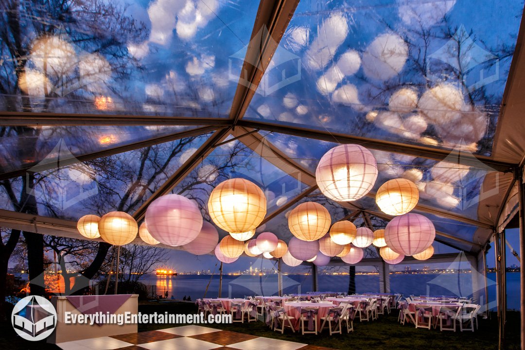 Interior view of a clear top tent with glowing paper lanterns and harbor views at Alice Austen House by Everything Entertainment.